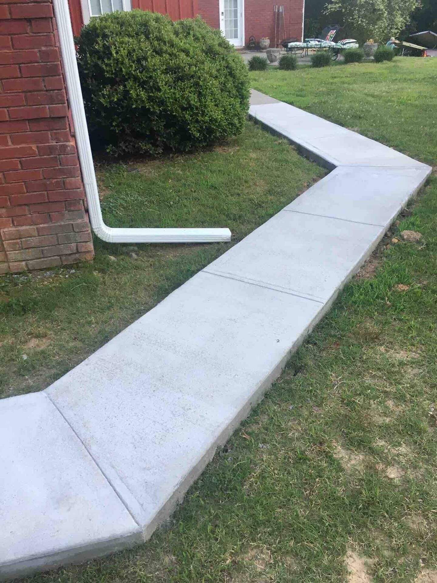 A concrete pathway leading to a brick building with a white door.