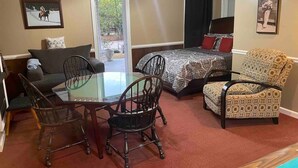 A room with a glass dining table, two chairs, a sofa, a patterned armchair, a bed with a patterned bedspread, and a ceiling fan. - Hank Williams hang out (Camden)