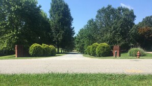 A gravel driveway leading to a brick entrance gate, surrounded by well-maintained hedges and trees. - Hank Williams hang out (Camden)