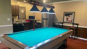 A pool table in a room with a kitchen area, a dining table, and a framed picture on the wall. - Hank Williams hang out (Camden)