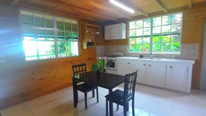 A wooden cabin with a dining area, kitchen, and large windows. - Tranquility Suite- Cottage 7 (Pointe Michel)