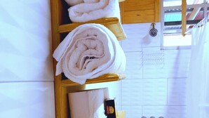 A bathroom with wooden shelves holding towels, a shower, and a tiled floor. - Tranquility Suite- Cottage 7 (Pointe Michel)