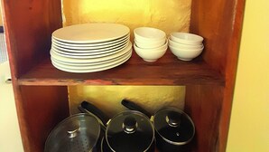 Une étagère en bois sur laquelle sont empilées des assiettes blanches, des bols et trois pots noirs avec des couvercles.