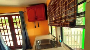 Une cuisine équipée d’un évier, d’une fenêtre donnant sur un espace verdoyant et d’un meuble rouge.