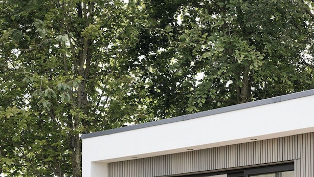 Un edificio moderno con amplios ventanales de vidrio, una cama con una manta roja y un jardín con plantas y una mesa.