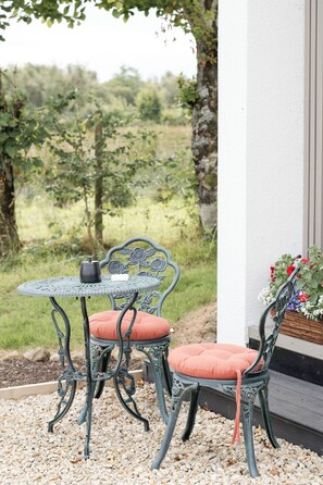 A patio with two metal chairs and a table, surrounded by pebbles and a view of a vineyard.