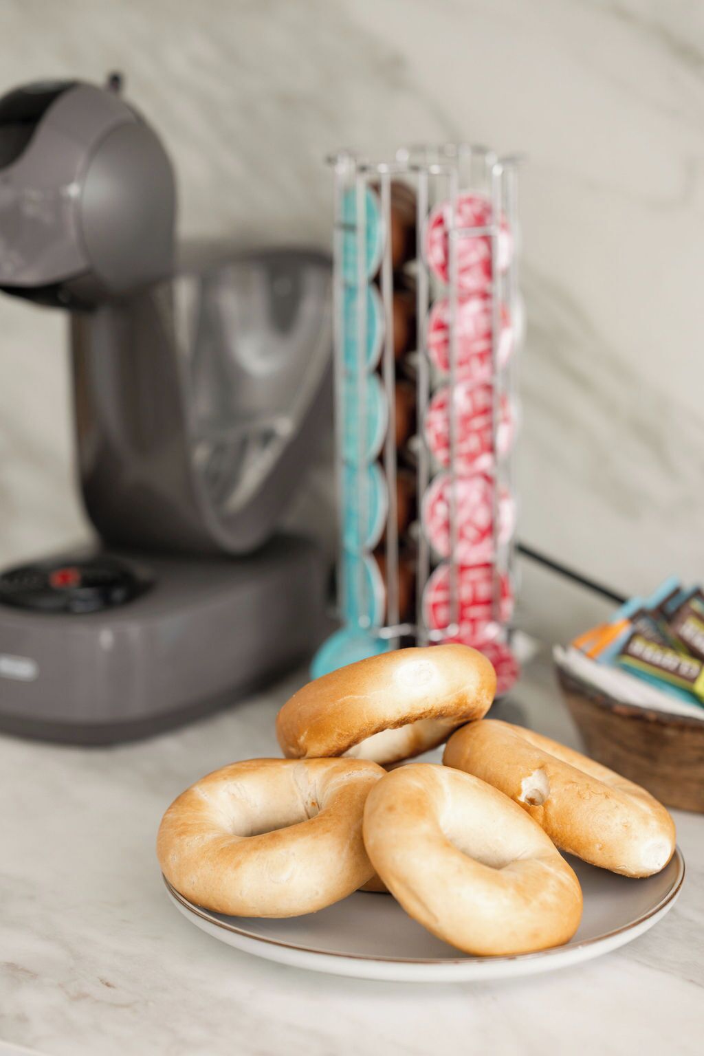 A plate of bagels with a stand of packaged donuts in the background.