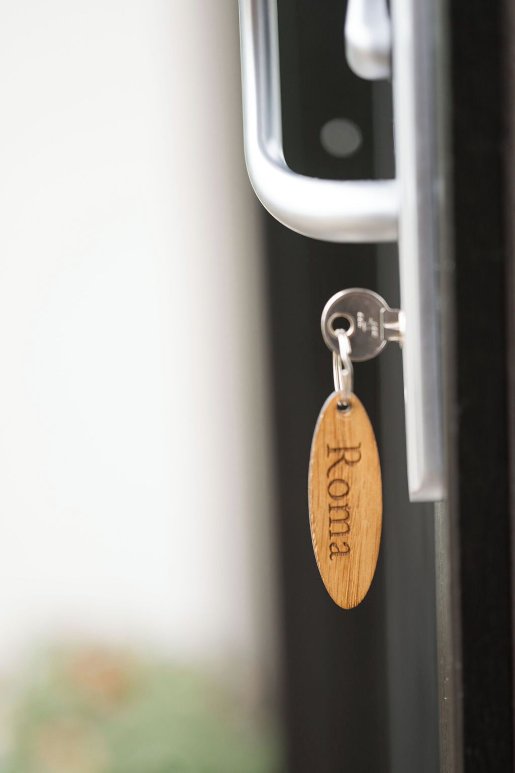 A keychain with the name "Roma" engraved on it, attached to a door handle.