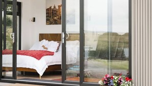 Un dormitorio con cama, un cuadro y vistas a través de un ventanal.