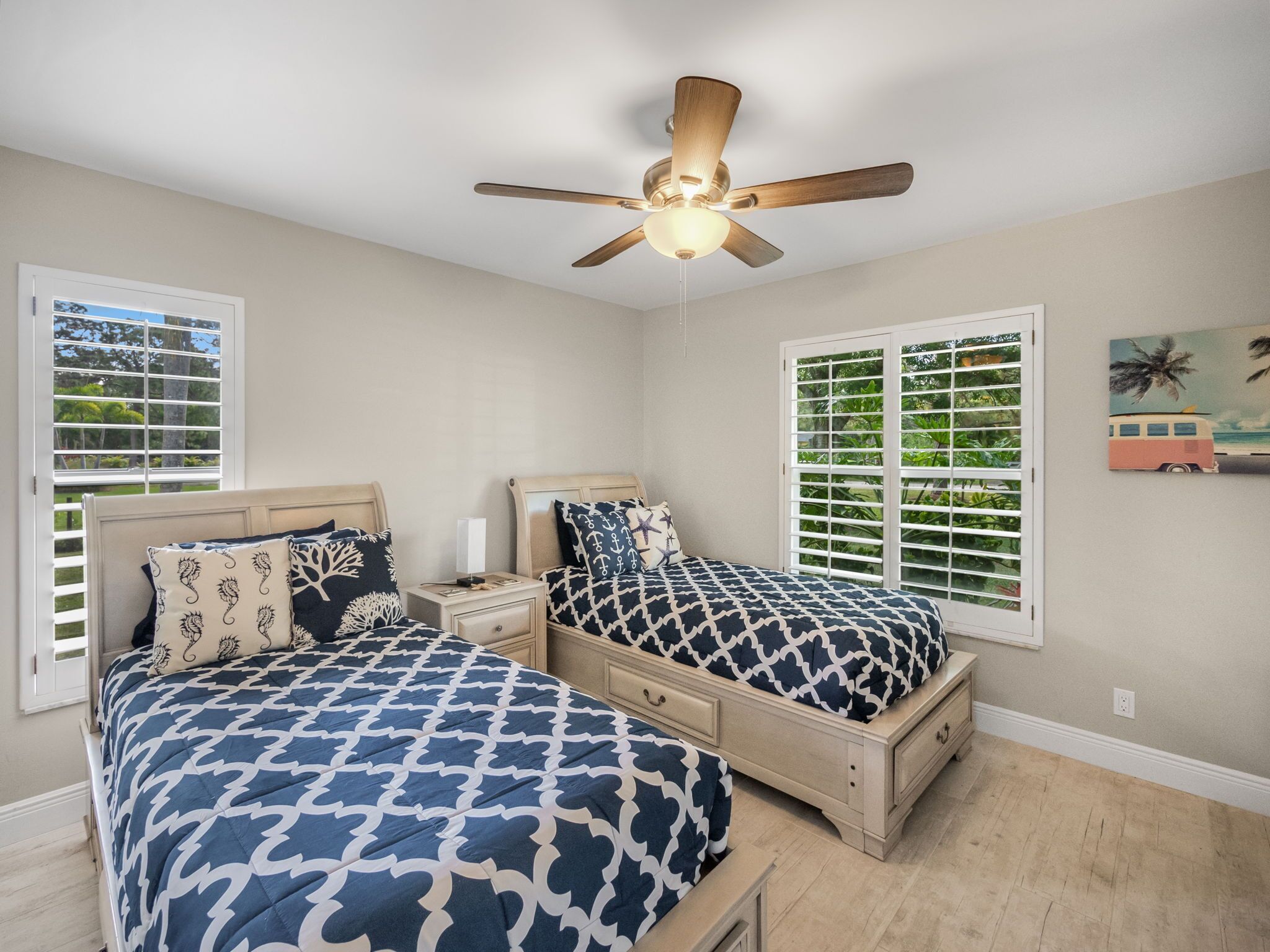 A bedroom with two beds, a ceiling fan, and a window with shutters.