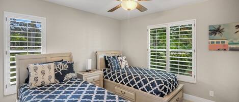 A bedroom with two beds, a ceiling fan, and a window with shutters.