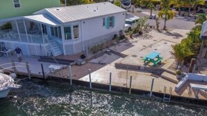 A small, single-story house with a covered porch and a small deck, adjacent to a body of water. - Empty RV Lot with Amazing Views! (Cudjoe Key)