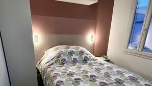 Ein kleines Schlafzimmer mit Bett, Nachttisch, Fenster und Kleiderschrank.
