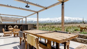 Une terrasse extérieure en bois, avec une table et des chaises, un mur en pierre et une vue sur des montagnes enneigées.