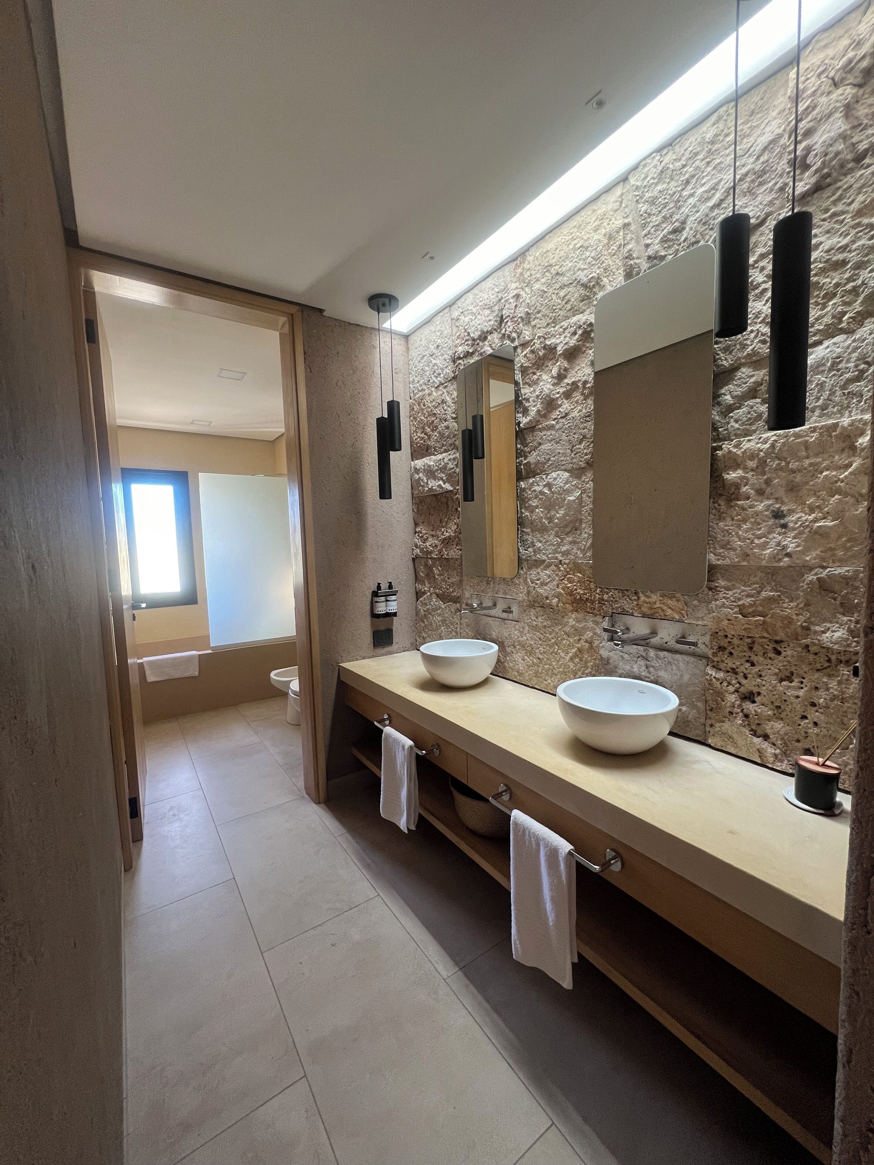 A modern bathroom with two large sinks, a stone wall, and a skylight.