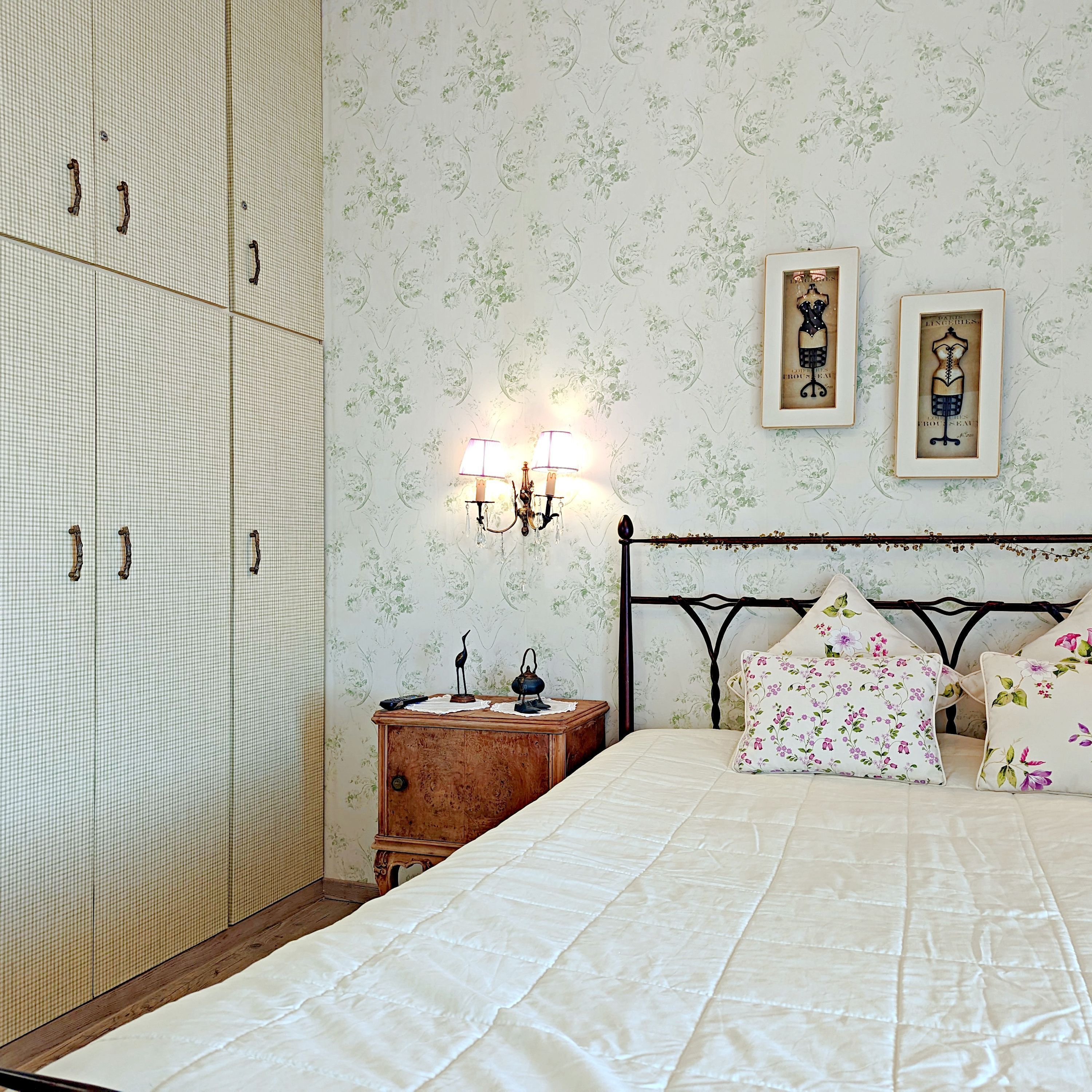 A bedroom with a bed, a wardrobe, a nightstand, and two wall-mounted lamps.