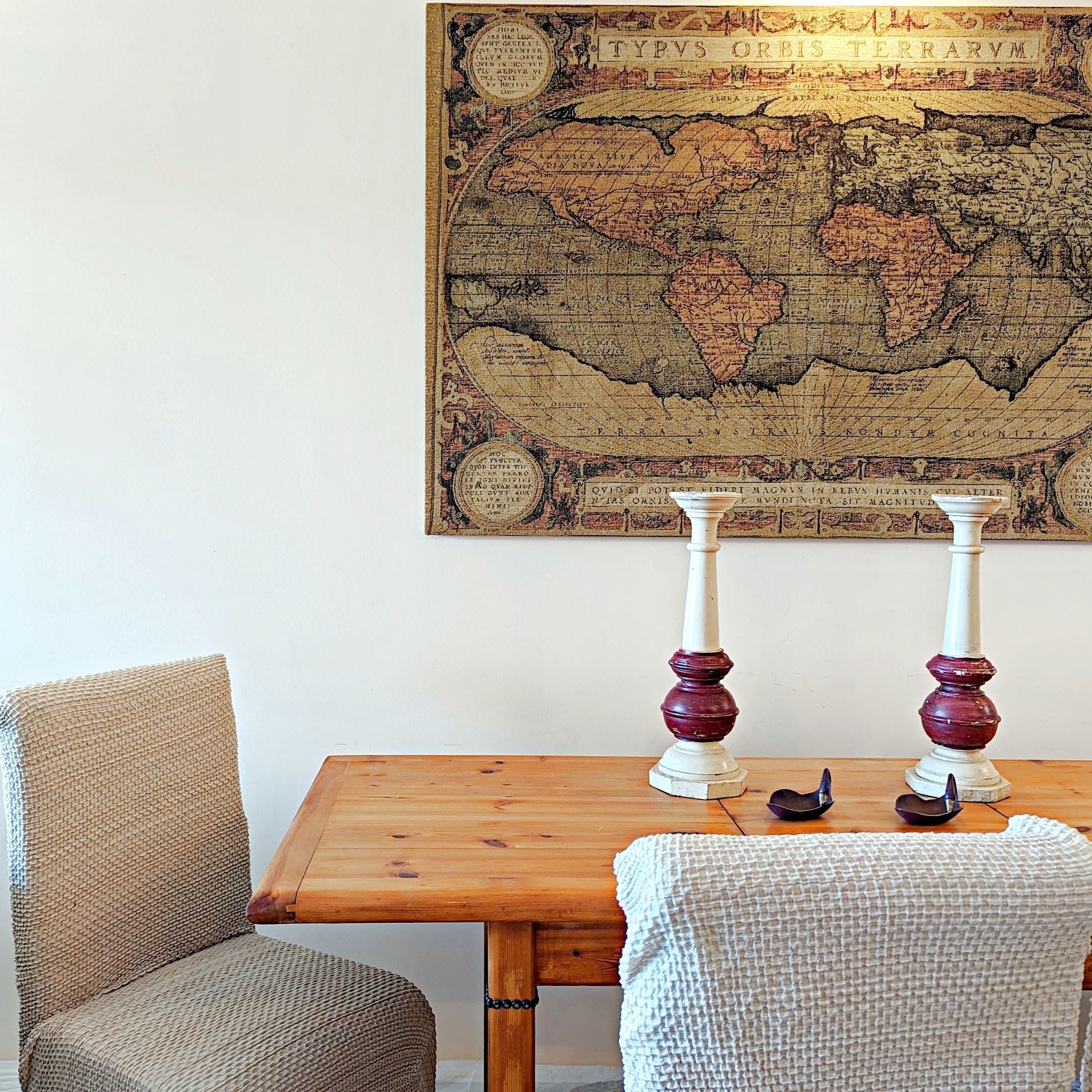 A wooden table with two candlesticks, a woven chair, and a wall-mounted map.