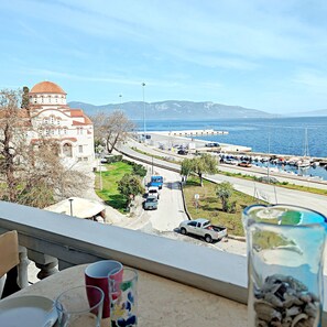 Blick vom Balkon auf eine Küstenstraße mit einem historischen Gebäude und einem Yachthafen.