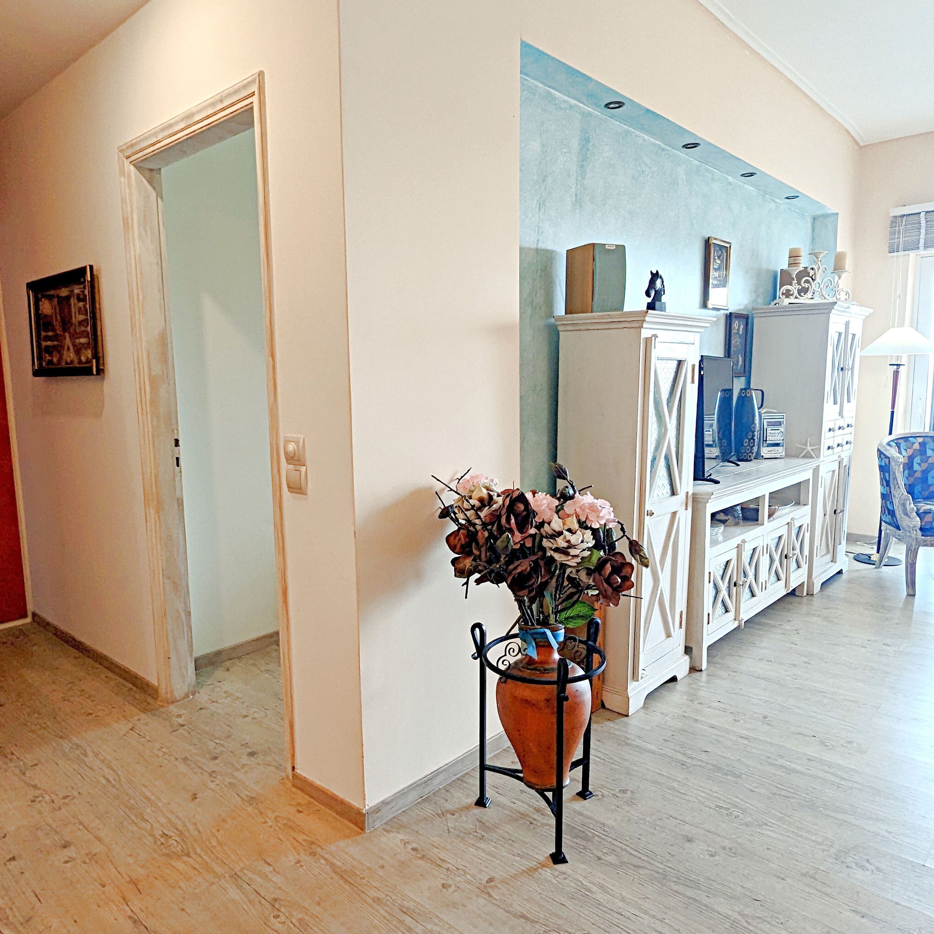 A hallway with a wooden floor, a white door, a blue wall, and a white cabinet with decorative items.