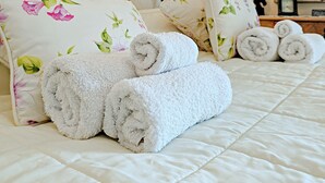 Ein ordentlich bezogenes Bett mit floralen Kissen und aufgerollten weißen Handtüchern.