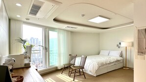 Habitación de hotel con cama, escritorio, silla, planta y vista a la ciudad.