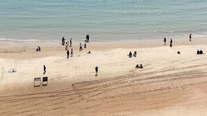 Una playa con gente dispersa a lo largo de la orilla, un arco de fútbol y un puesto de socorristas.