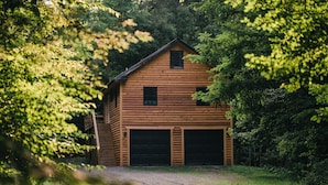 En træhytte med to garageporte, omgivet af tæt skov.
