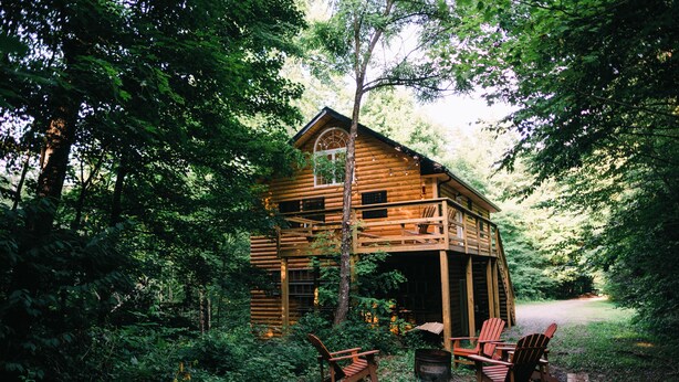 En træhytte omgivet af tæt skov, med en veranda og to Adirondack-stole.
