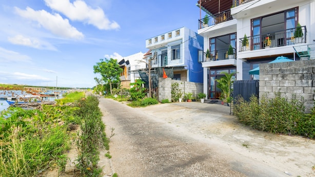 Ein modernes Hotel mit einem Betonweg, der zum Eingang führt, umgeben von üppiger Vegetation und blauem Himmel.