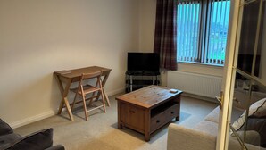 Una sala de estar con una mesa de madera, un televisor, un sofá y una ventana con cortinas.