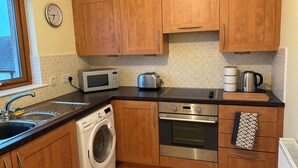 Una cocina compacta con armarios de madera, microondas, tostadora, hervidor, lavadora y horno.