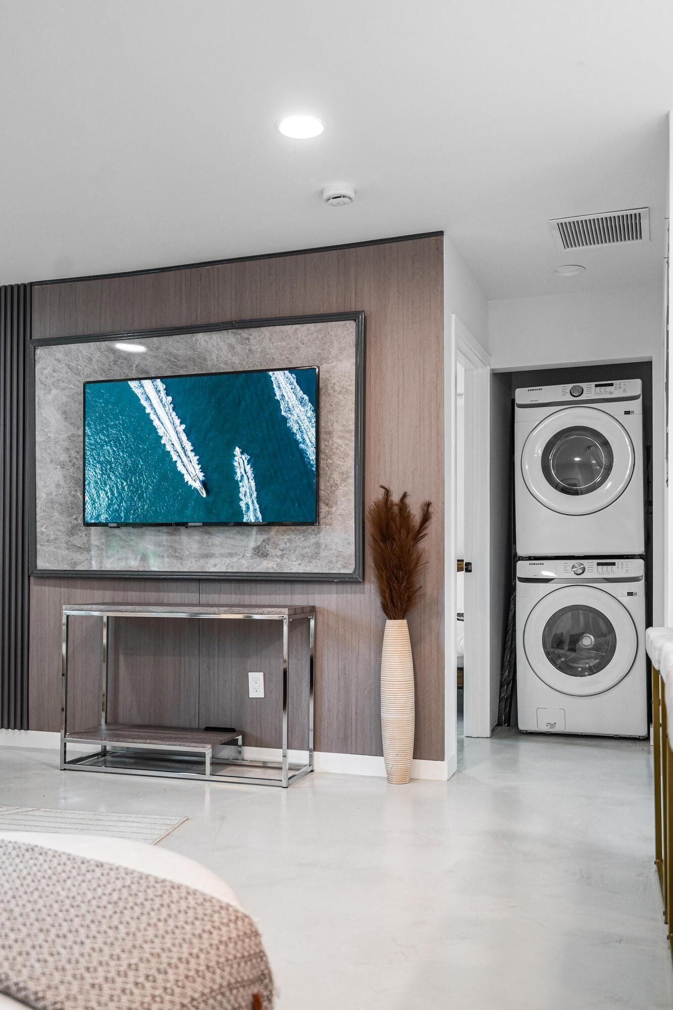 A modern living room with a flat-screen TV mounted on a wooden wall, a built-in washer and dryer, and a minimalist console table.