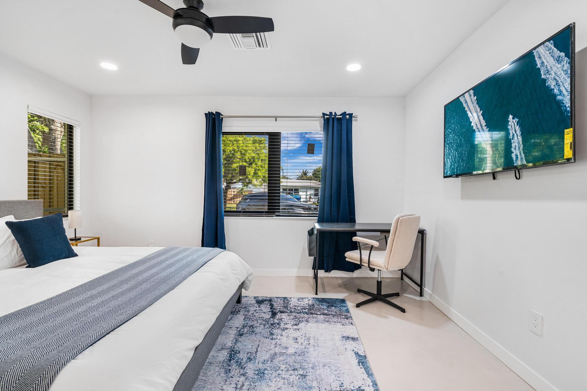 A modern bedroom with a bed, desk, chair, and a large window with curtains.