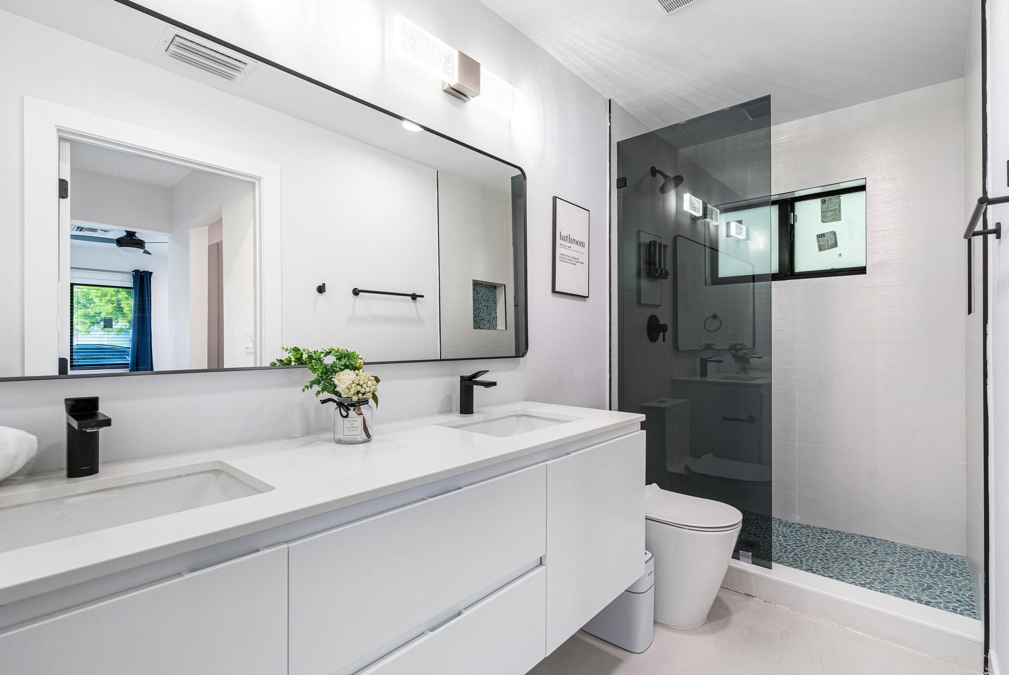 Une salle de bain moderne avec deux lavabos, un grand miroir et une douche à parois de verre.
