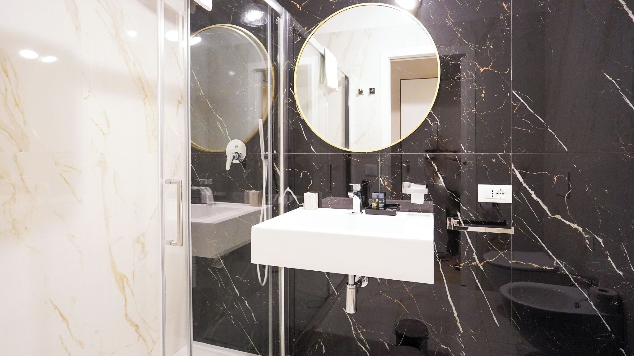 A modern bathroom with a glass-enclosed shower, a white sink, and a large mirror with a gold frame.