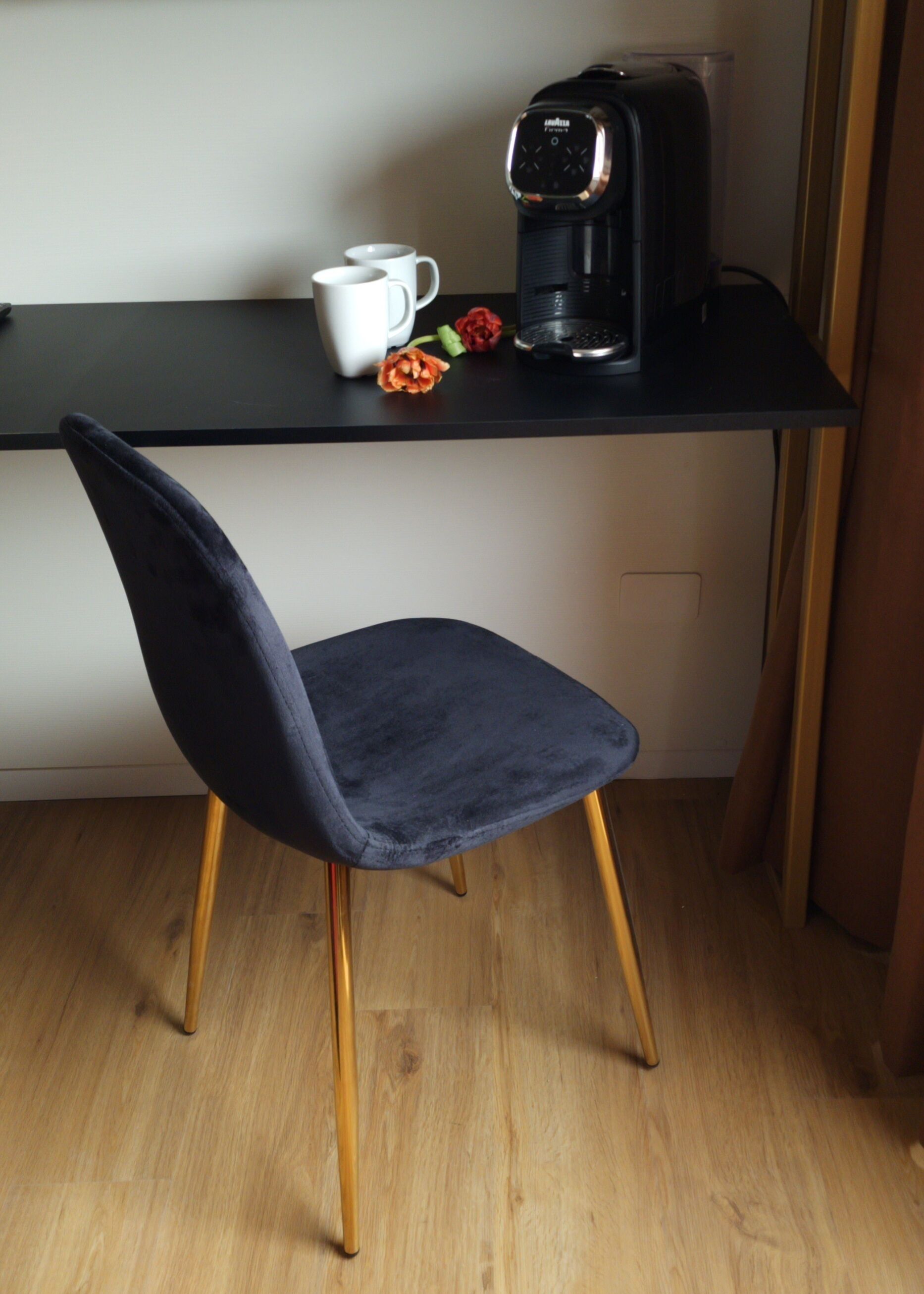 A dark blue chair with wooden legs, a black coffee maker, and a white mug on a black desk.
