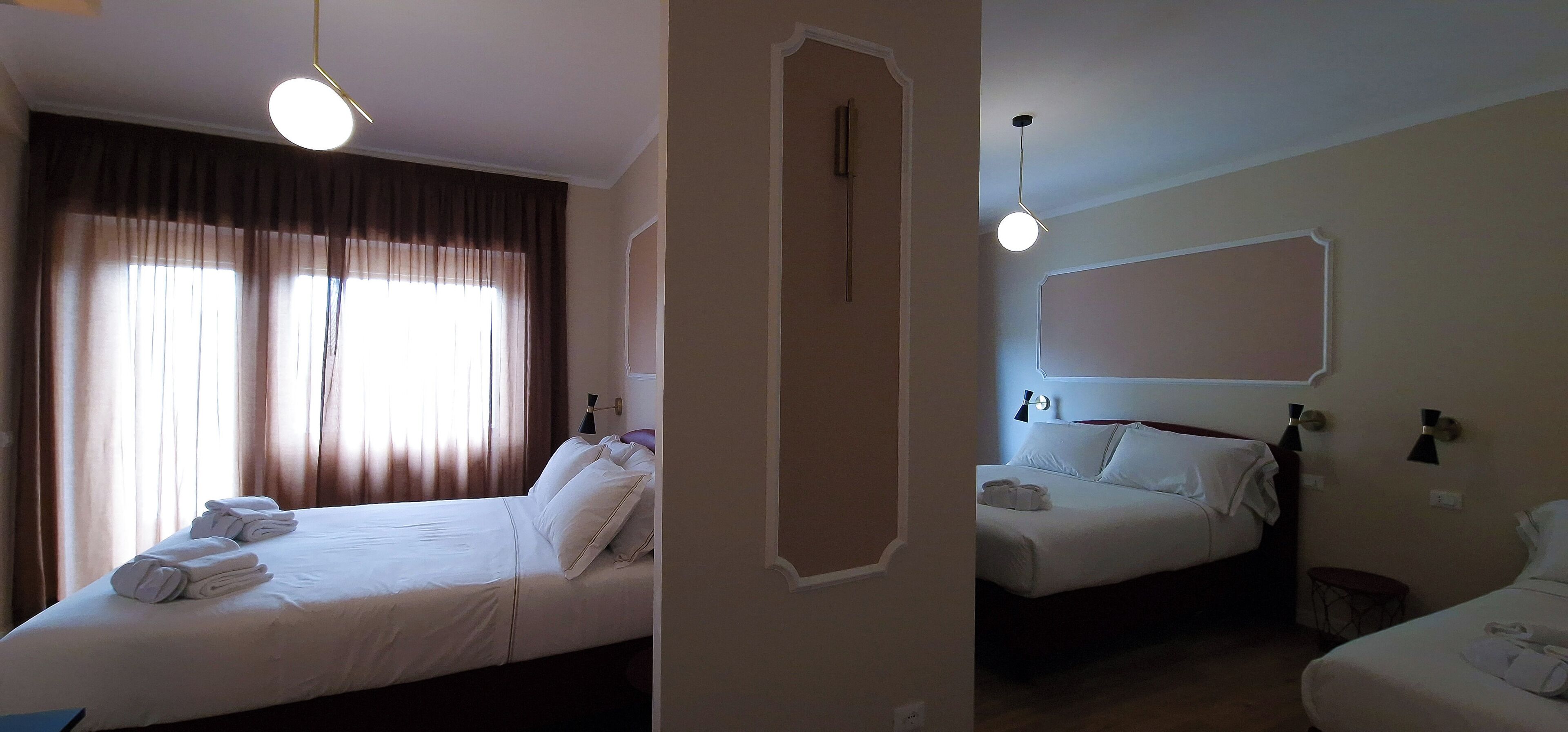 A hotel room with two beds, a large window with curtains, and a wall-mounted mirror.