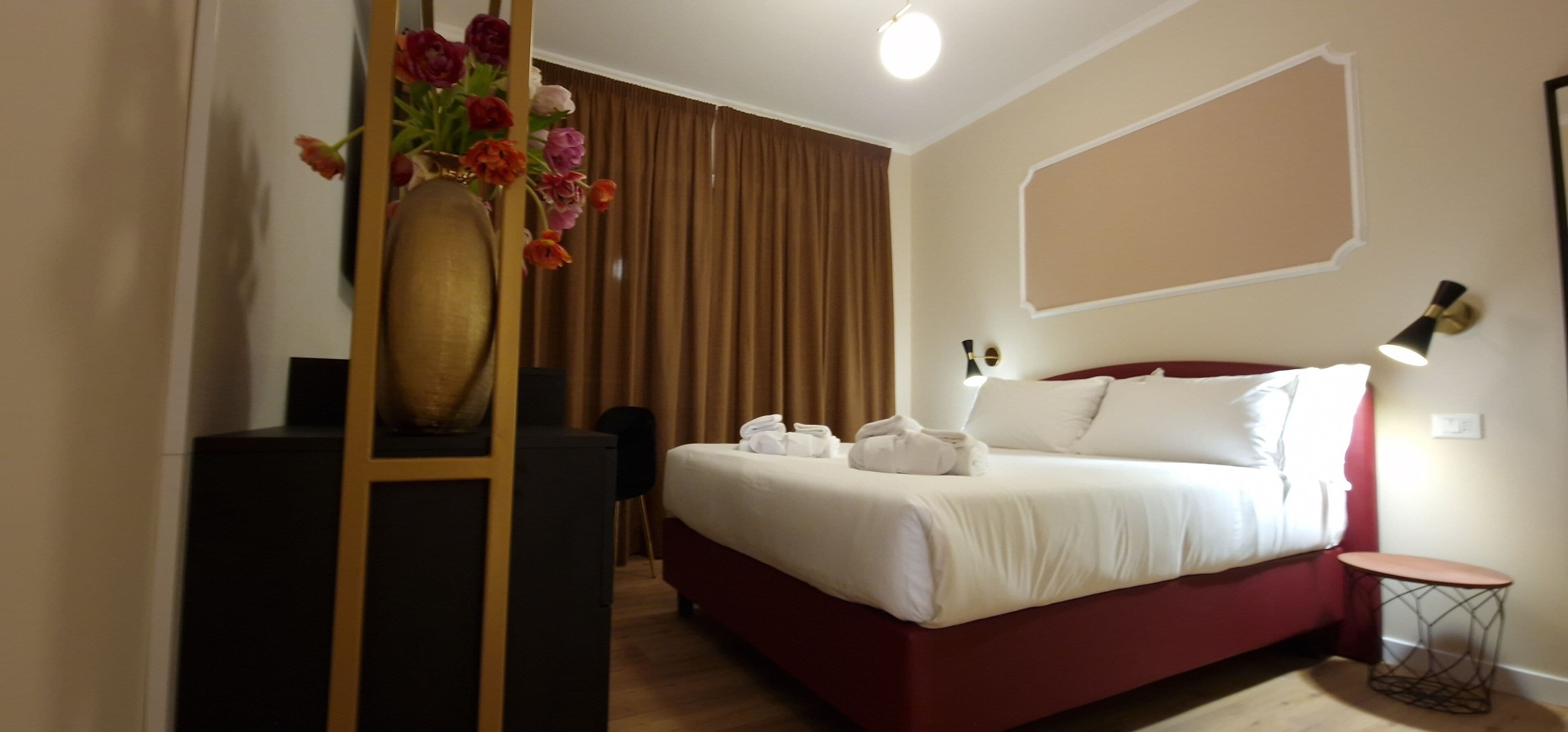 Ein Hotelzimmer mit Bett, Schreibtisch, Stuhl, einer Blumenvase und einer Lampe.