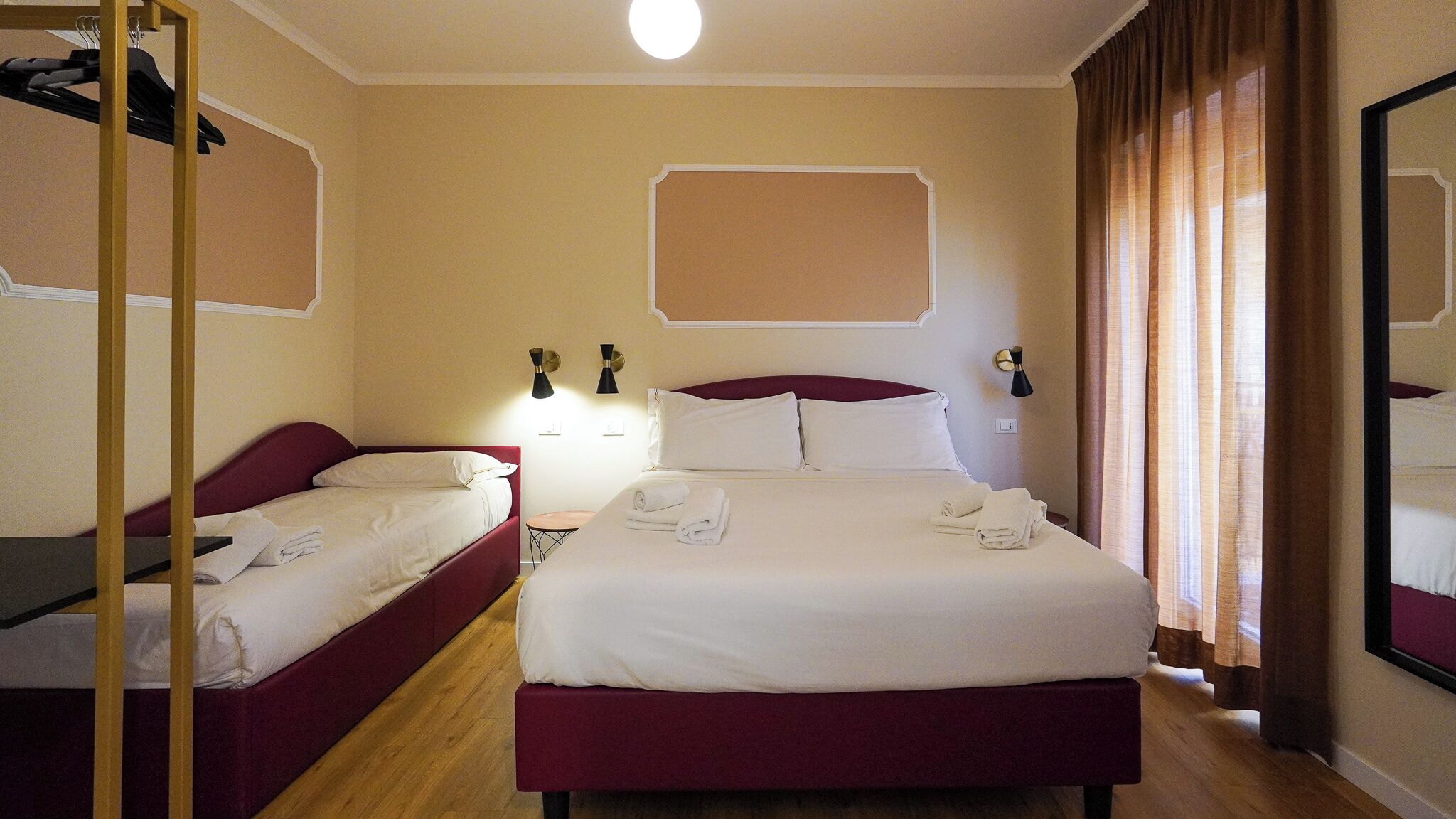 Quarto de hotel com duas camas, piso de madeira e um espelho grande em uma parede.