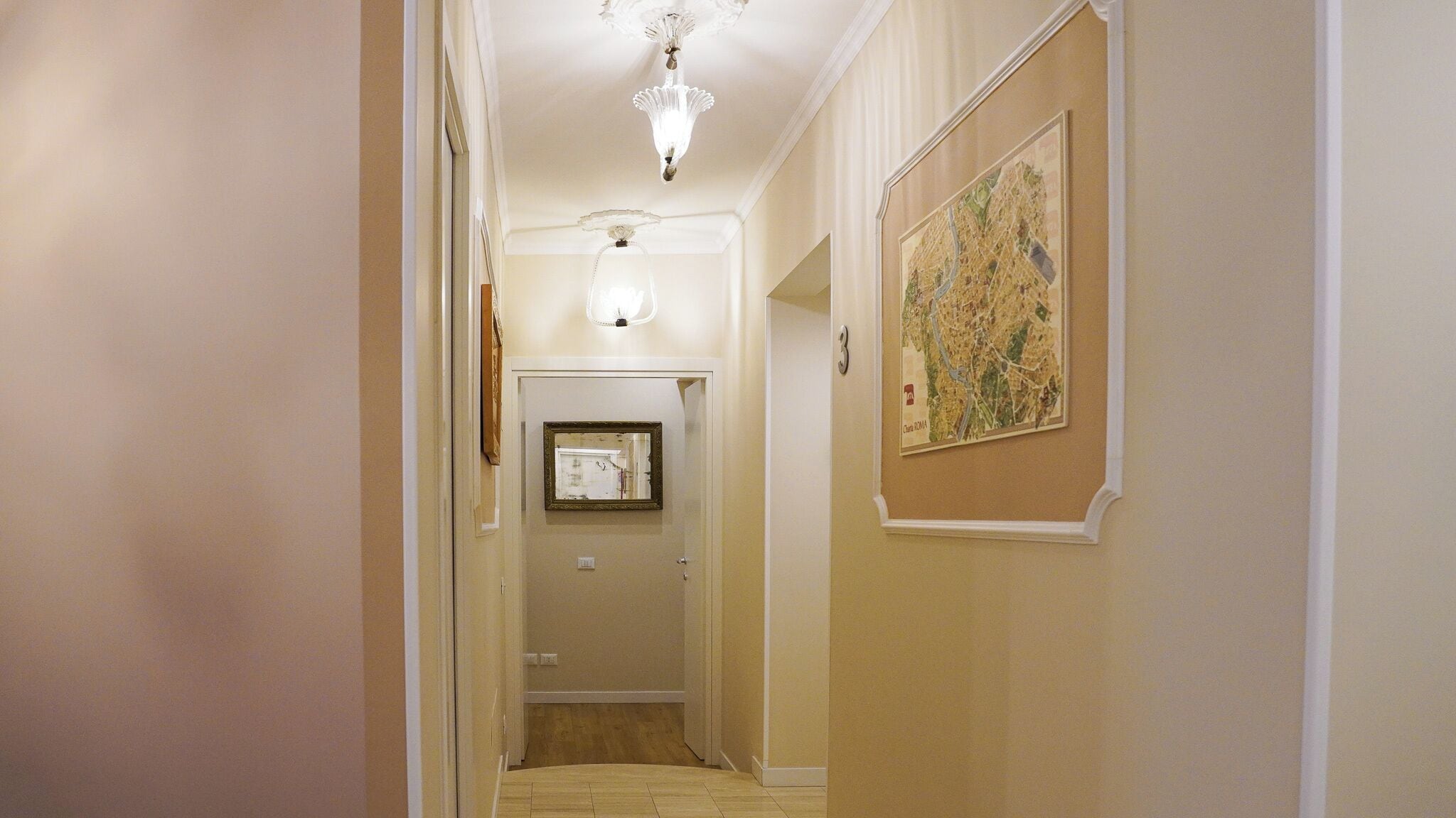 A hallway with a chandelier, a framed mirror, and a map on the wall.