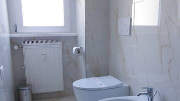 A modern bathroom with two sinks, a toilet, a window, and a mirror with a vase of flowers.