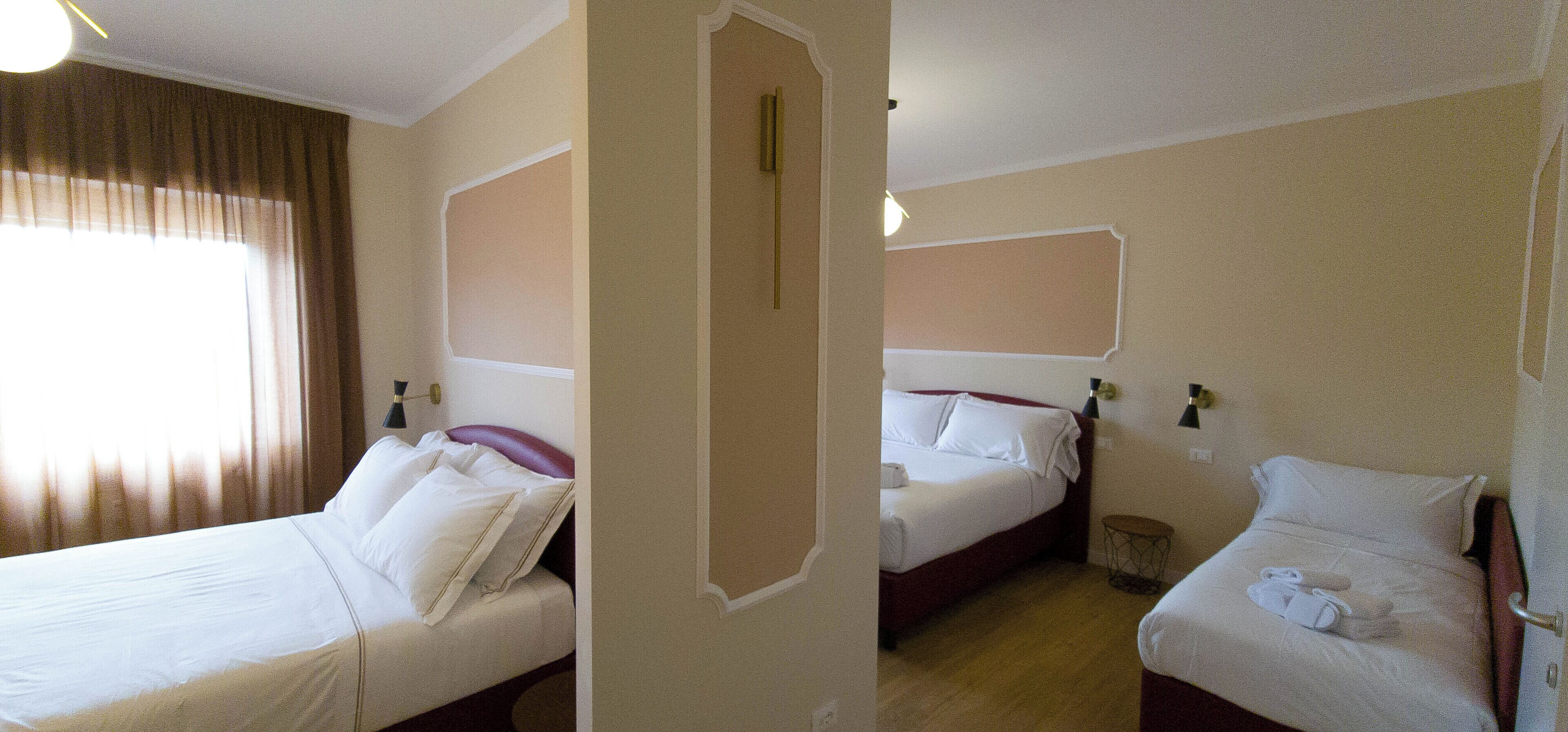 A hotel room with two beds, a small bedside table, a lamp, and a window with curtains.
