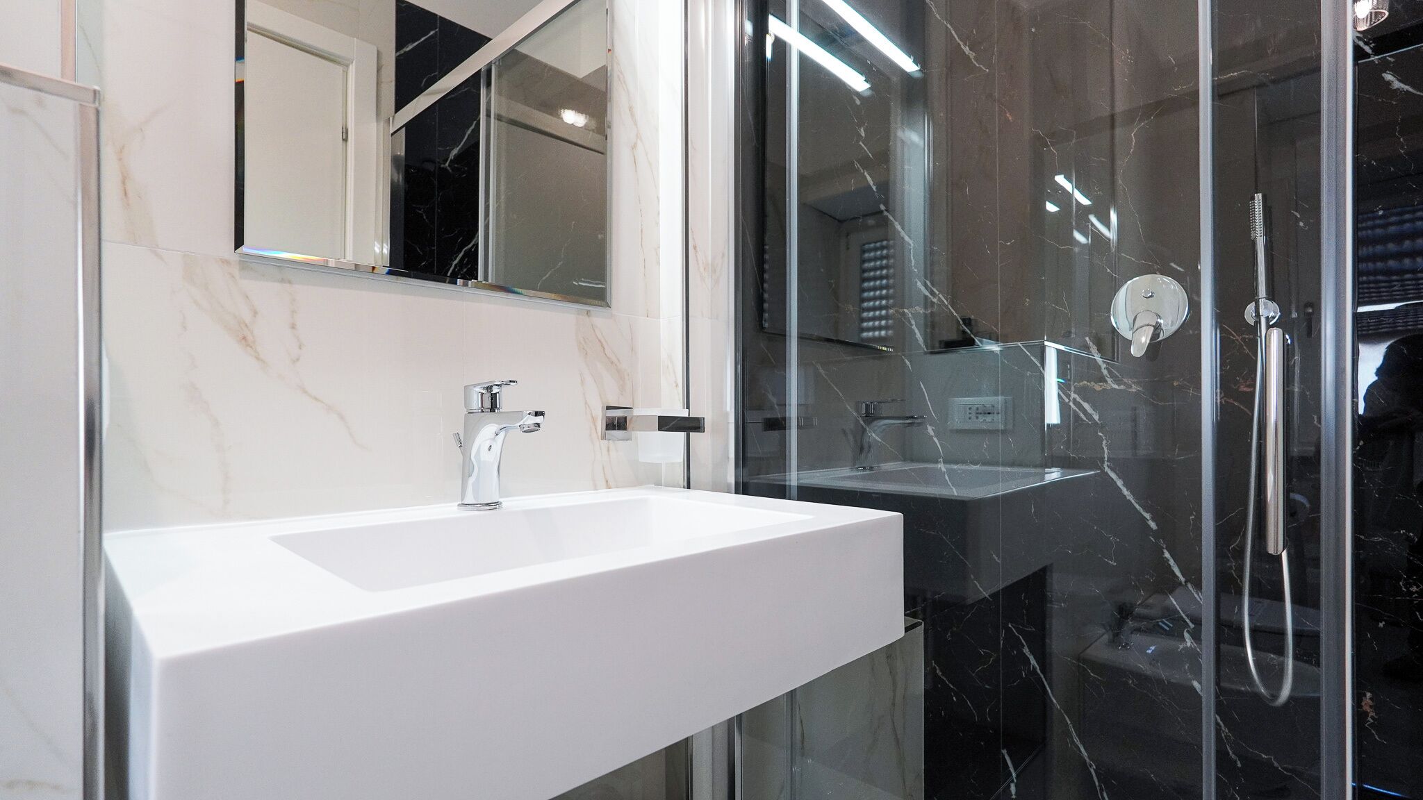 Une salle de bain moderne avec un lavabo blanc, une douche en verre et un pare-baignoire en marbre.