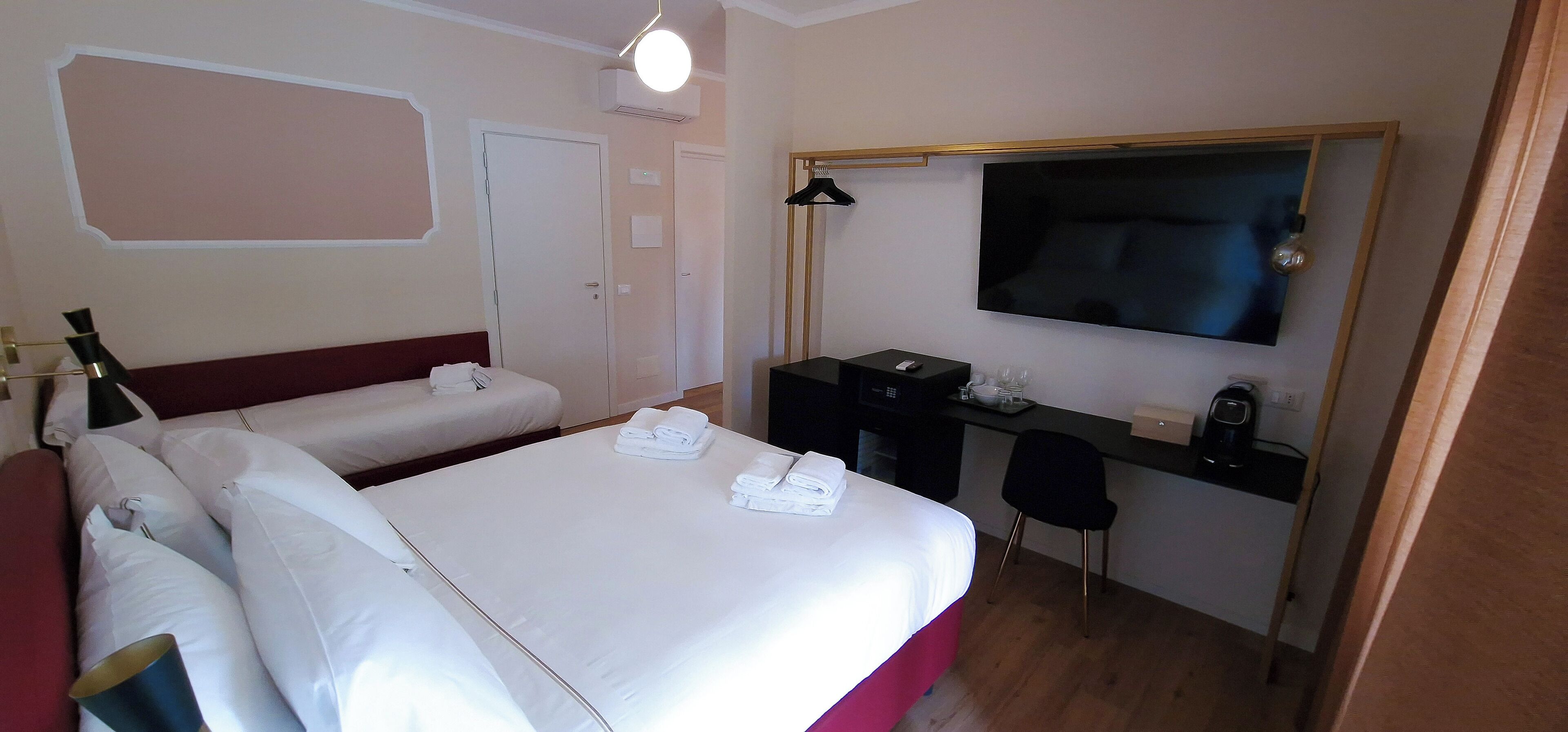 A hotel room with a bed, a desk, a chair, a TV, and a coat rack.