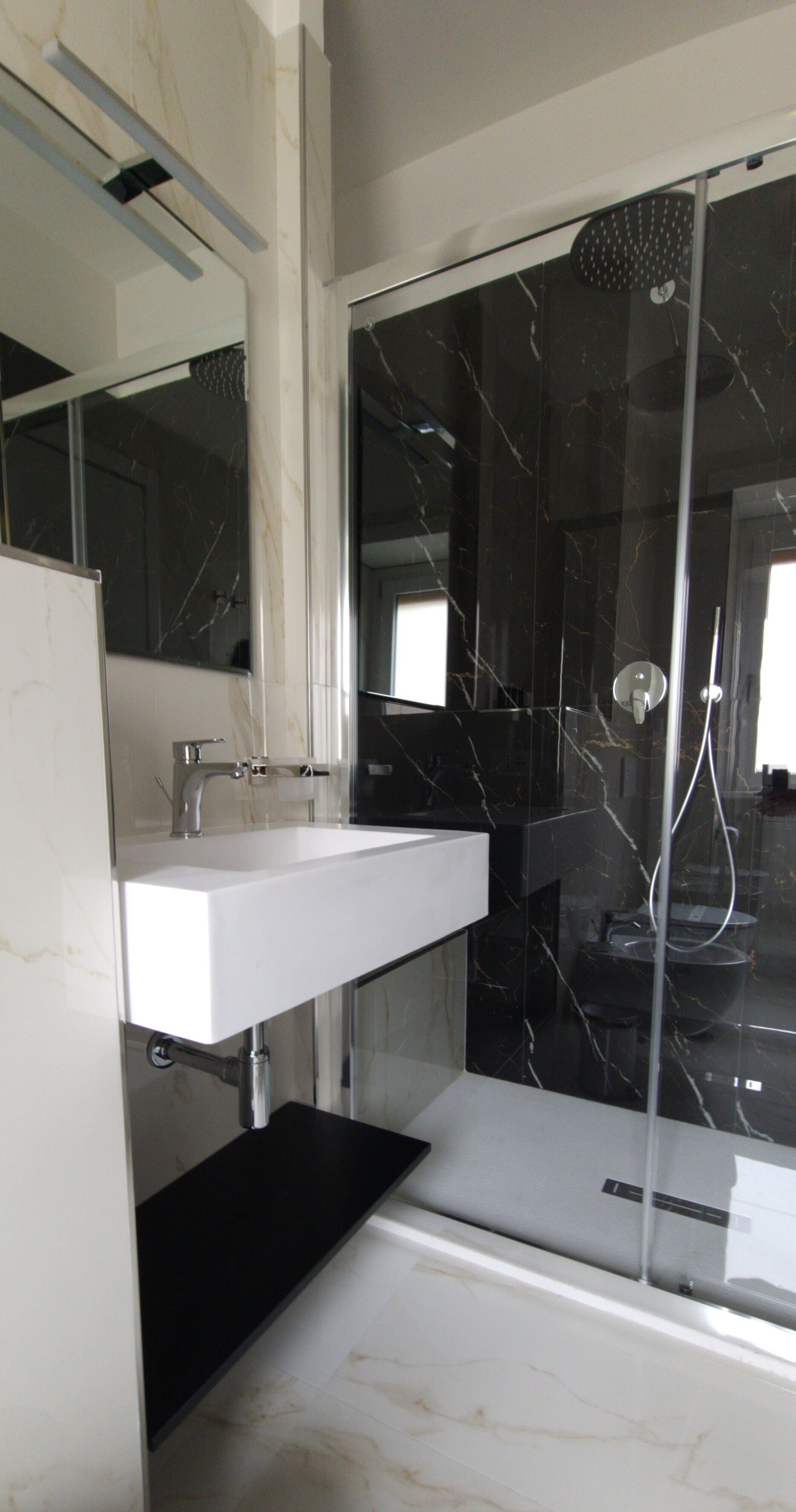 A modern bathroom with a white sink, a glass shower enclosure, and a marble-tiled floor.