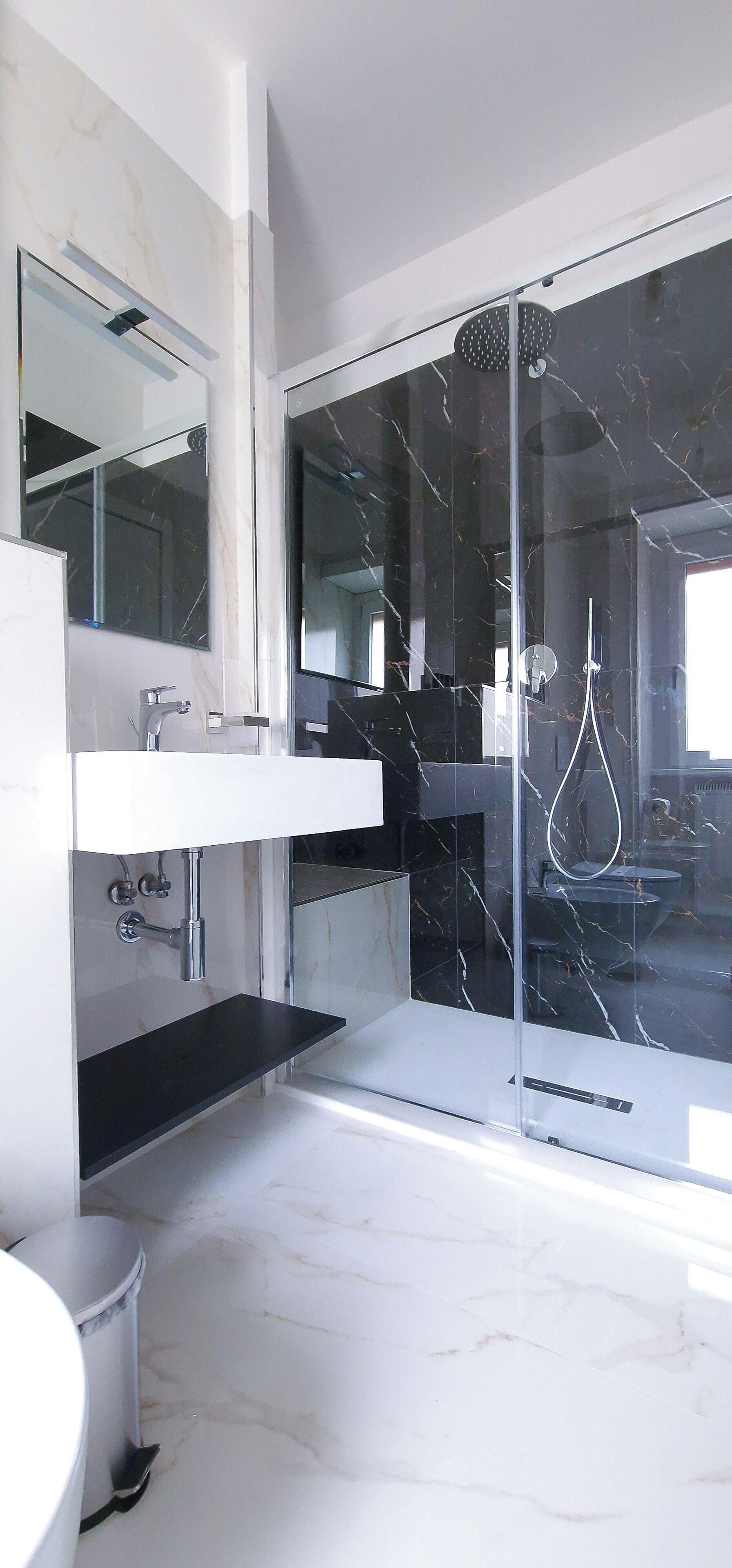 A modern bathroom with a glass-enclosed shower, a white marble sink, and a large mirror.