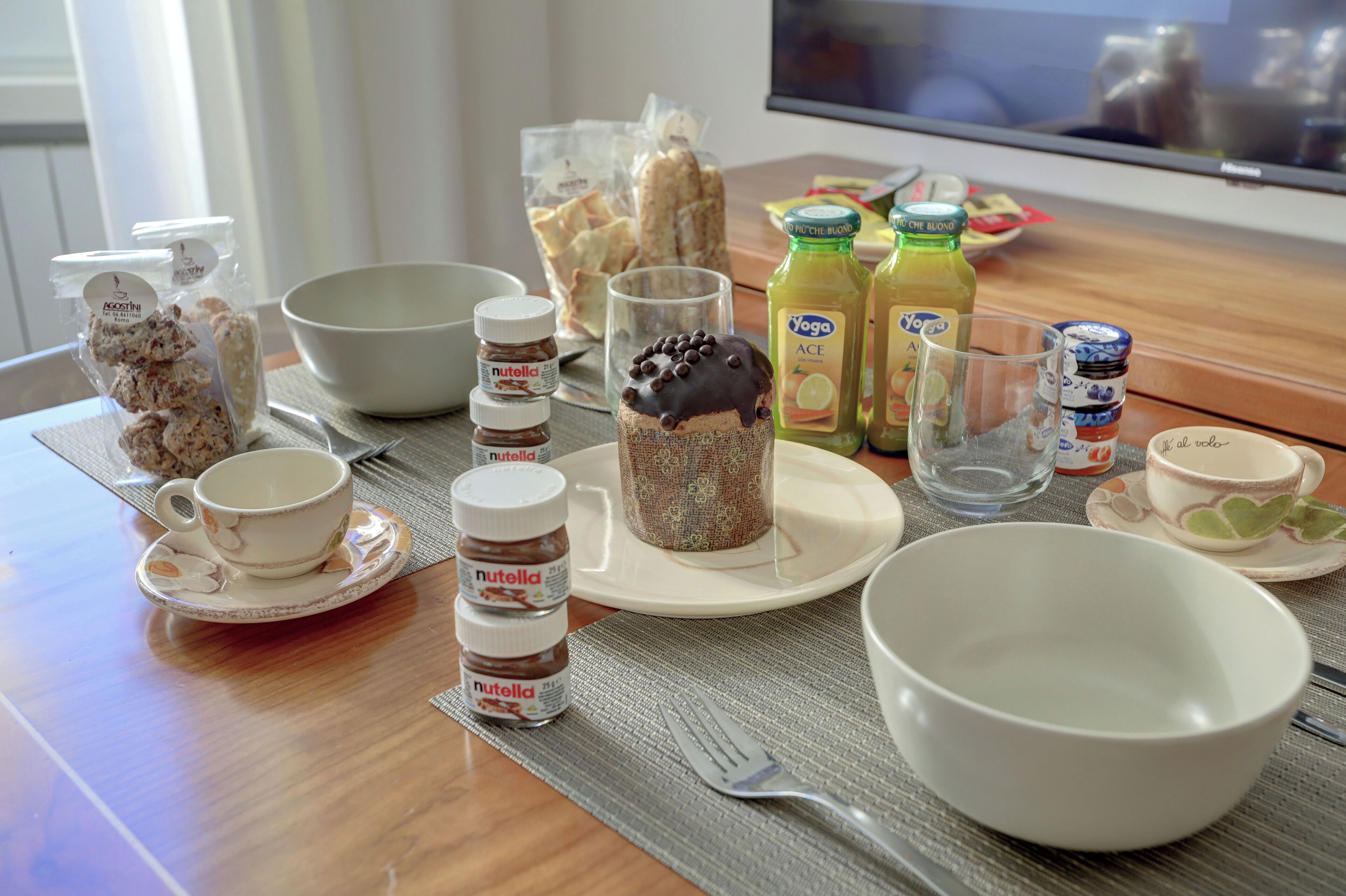 Ein Esstisch mit verschiedenen Speisen, darunter Gläser Nutella, eine Torte mit Schokoladenguss und Saftflaschen.
