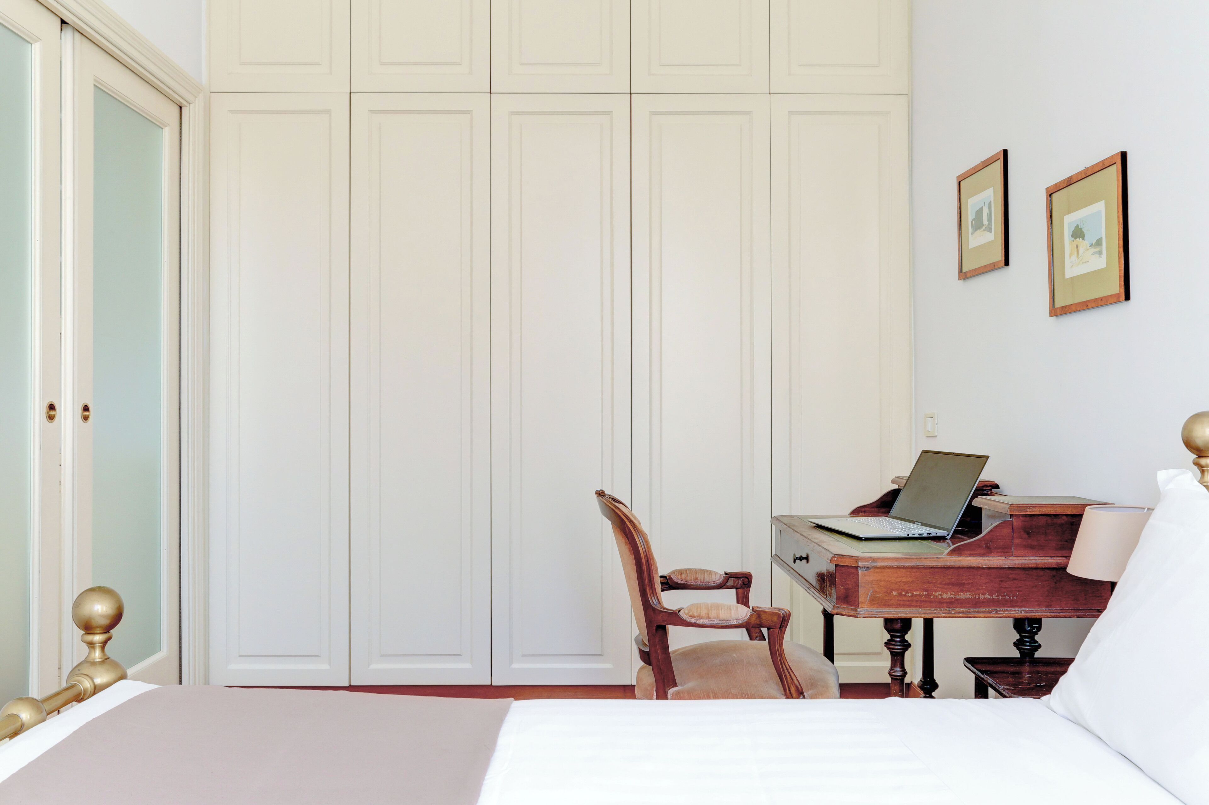 Un dormitorio con una cama, un escritorio de madera con una computadora portátil, una silla y un armario.