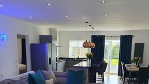 A modern living room with a grey sectional sofa, a wooden coffee table, and a dining area with a table and chairs. - Blue Bay Villa in Trearddur Anglesey (Trearddur Bay)