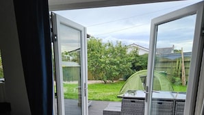 A room with a sliding glass door leading to an outdoor patio with a green tent and a wooden deck. - Blue Bay Villa in Trearddur Anglesey (Trearddur Bay)